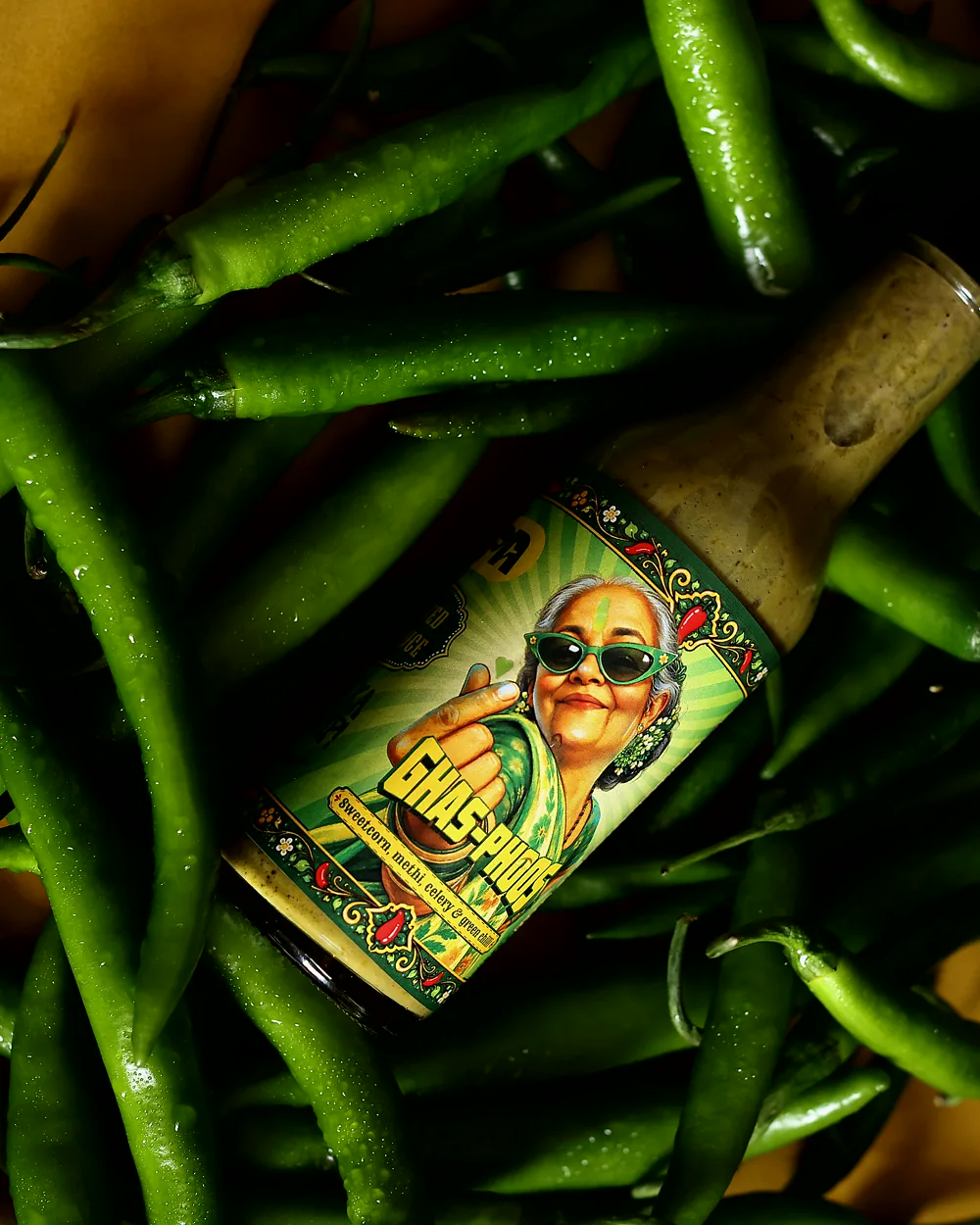 A bottle of Ghas Phoos lying on a bed of fresh green chillies